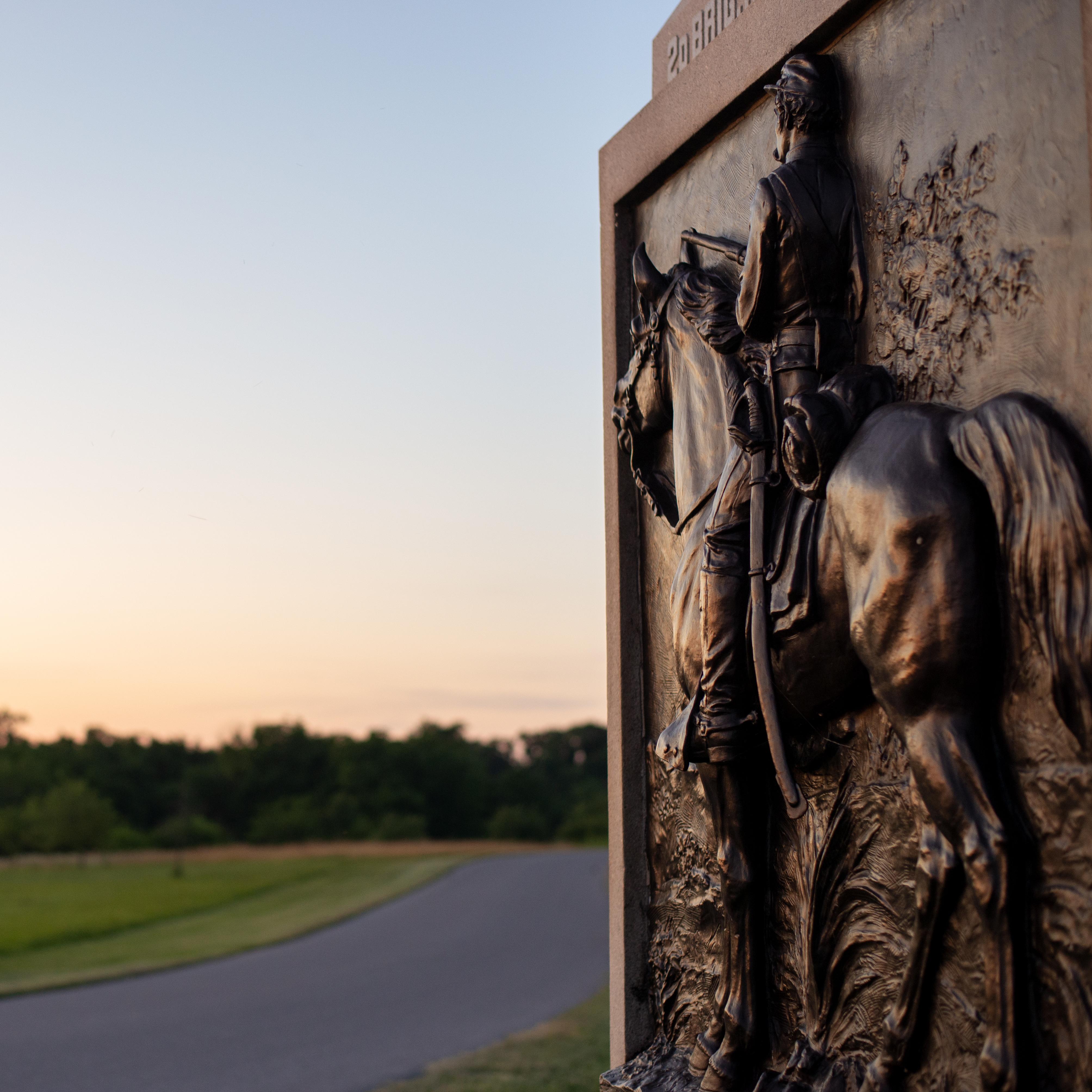 Bronze man on horse on monument with road in the background.