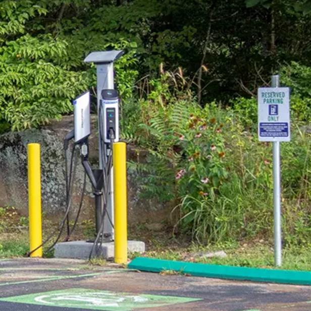 Man in jacket and hat plugging in car to electric vehicle charging station.