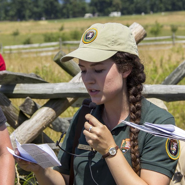National Park Service Volunteer tan hat and green shirt stands next to a park ranger.