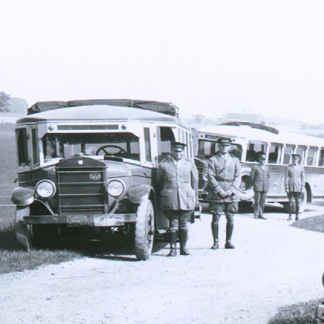 Black and white photograph of four buses, drivers, and Licensed Battlefield Guide circa late 1920s.