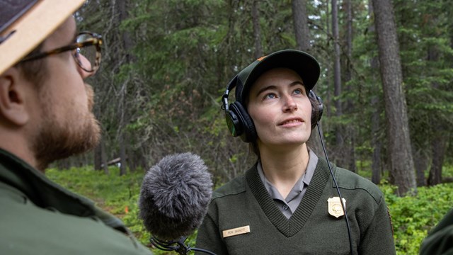 A woman in a park service uniform points a microphpone at a man in a ranger hat.