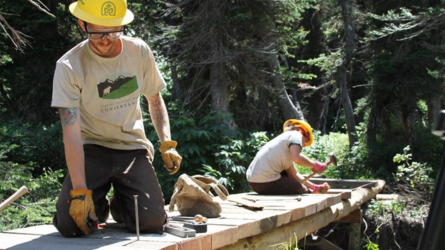 Trail workers in Conservancy t-shirt work on wood bridge