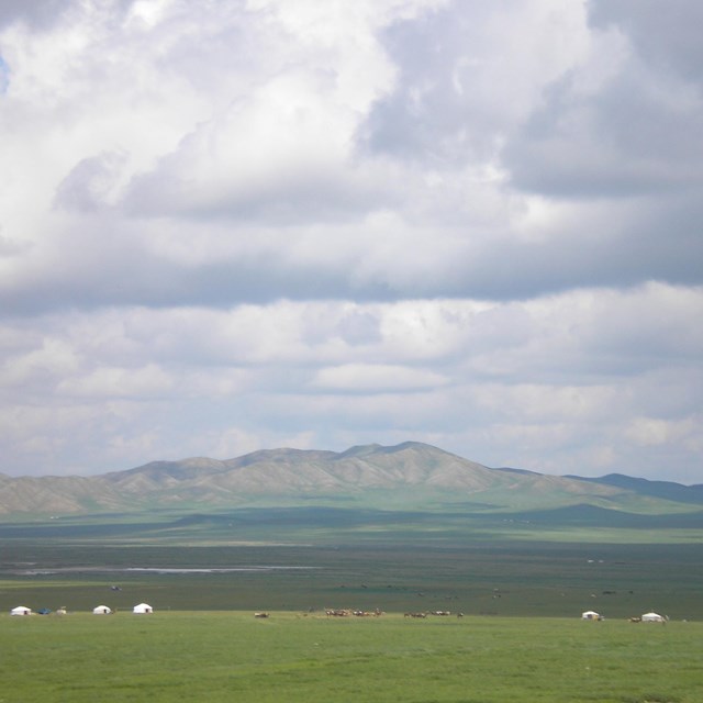 an expansive valley with mountains in the background and clouds in the sky.