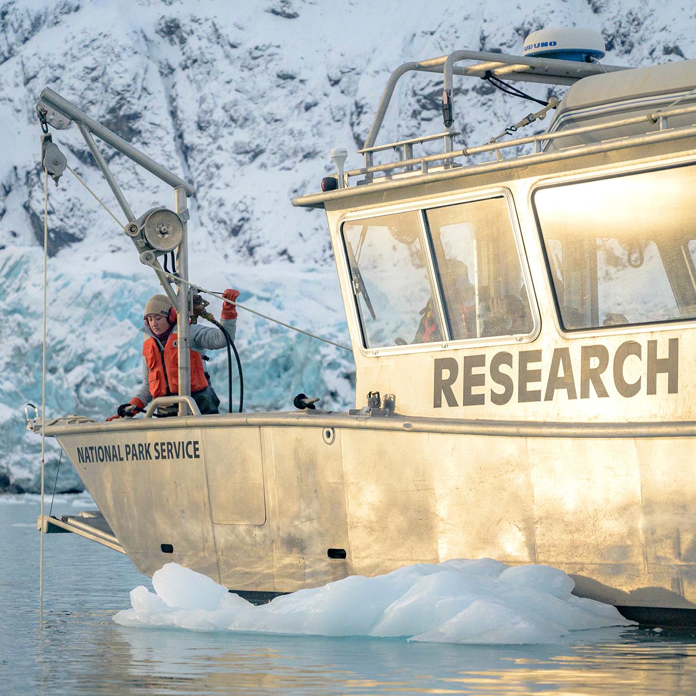 A park ranger works a rope pulley device on a research boat in front of Margerie Glacier