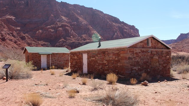 Two stone masonry buildings with green roofs. Sandstone canyon in background.