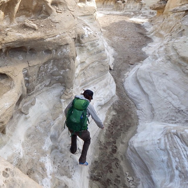 Hiker jumps down from rock shelf in slot canyon