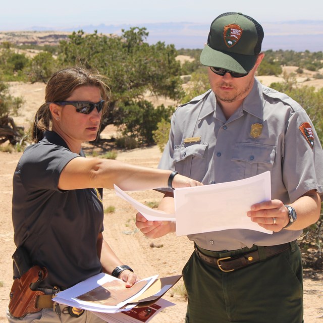 Two rangers discuss planning materials while standing on a mesa