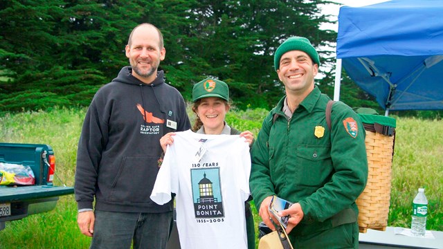 two rangers and raptor conservatory staff hold Point Bonita t-shirt