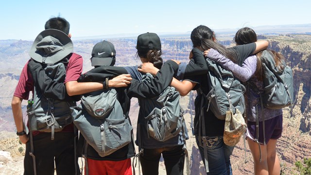 Students with arms over each other's shoulders, look out over Grand Canyon.