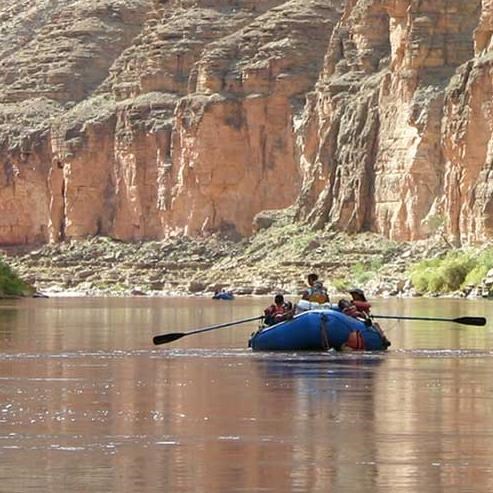 a blue raft floating on the Colorado River below towering cliffs.