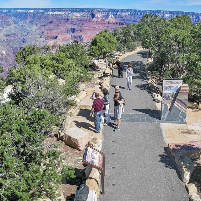 Park Visitors walking on a paved footpath along the edge of a vast and colorful canyon. 