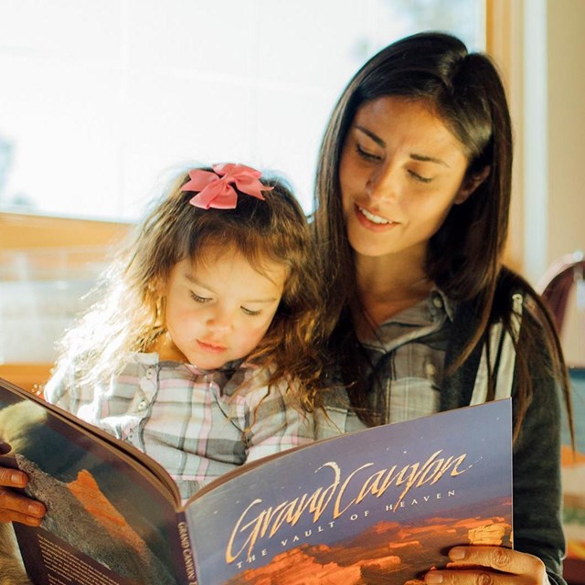 A woman is reading from a large picture book to her young daughter