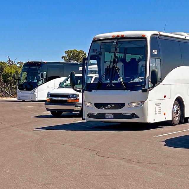 Two large tour buses and two transit vans are parked in a loading zone.