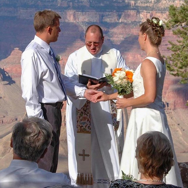 A minister is conducting a wedding ceremony with the couple standing to either side of him.