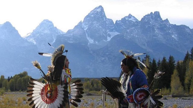Shoshone tribe members in regalia dancing with the Teton Range in the. distance