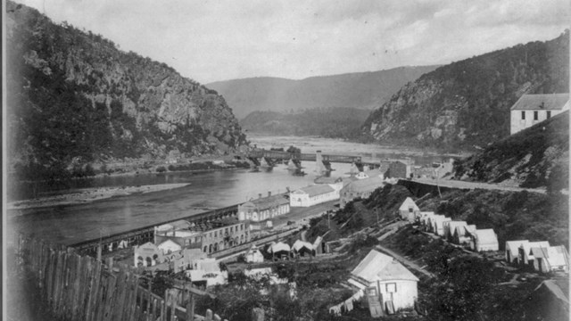 1860s black and white photo of Harper Ferry showing the mountains, gap, former armory grounds, etc.