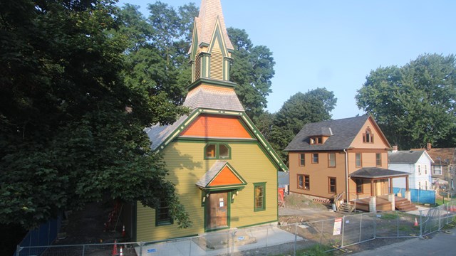 Street view of the front of the church and parsonage in summer with construction work visible.