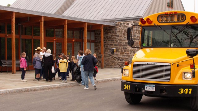 A school bus and students outside of the visitor center.