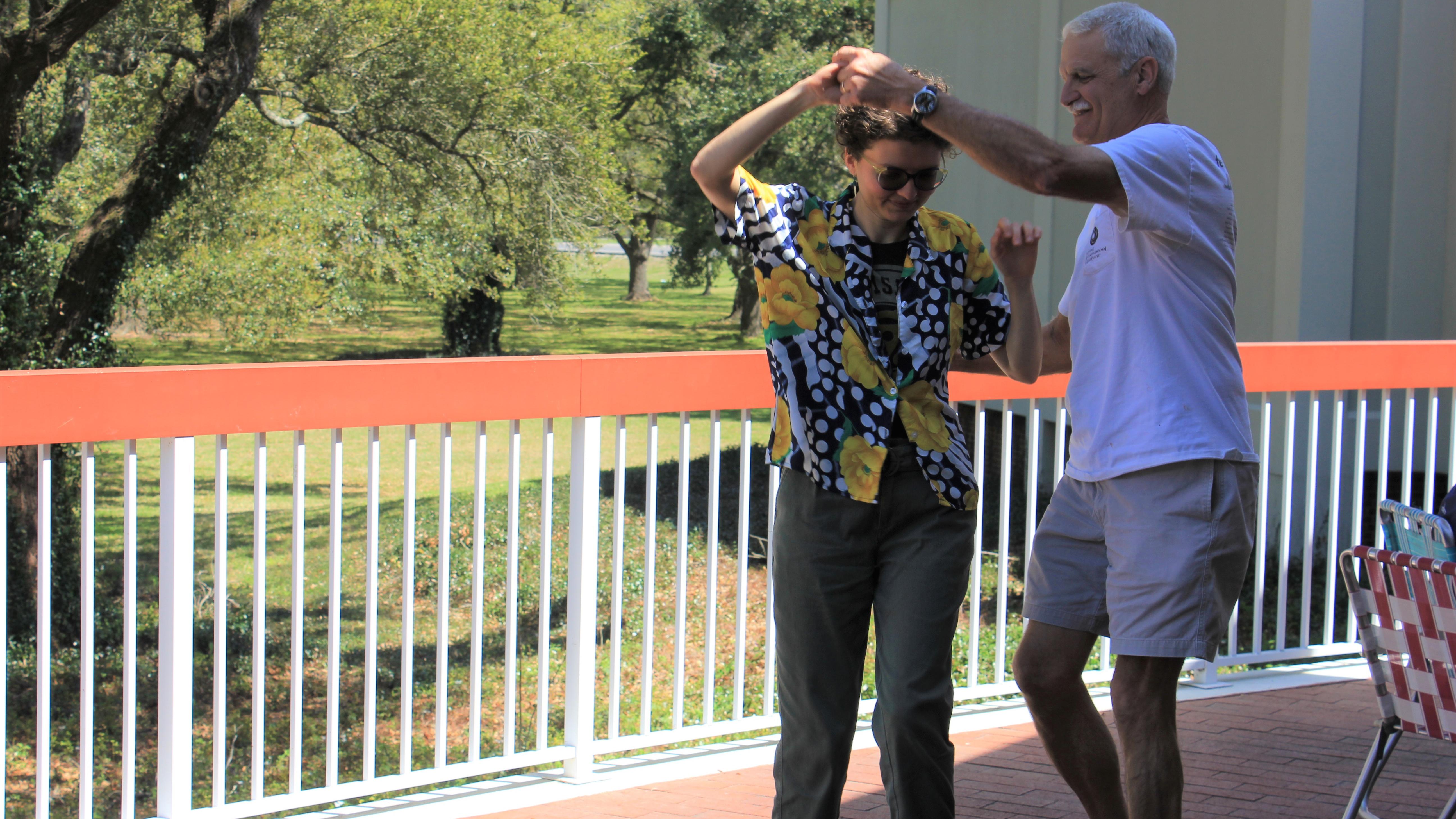 A man and woman hold hands and stand close together on a porch outside.