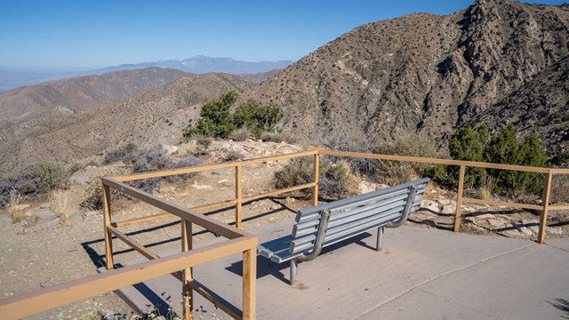 A bench surrounded by railing overlooks a mountain and valley.