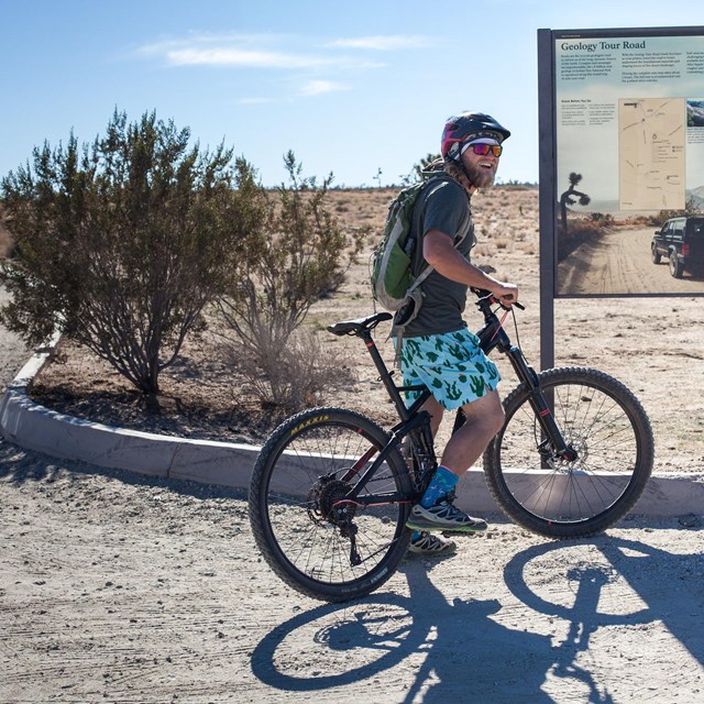 A mountain biker is stopped looking at the information panel about Geology Tour Road.