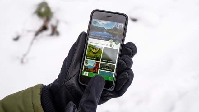 A close up photo of a person navigating the Katahdin Woods and Waters NM Page on the NPS App.