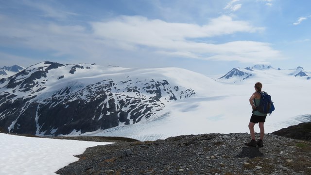 A hiker looks out over snow-covered glaciers and mountains.