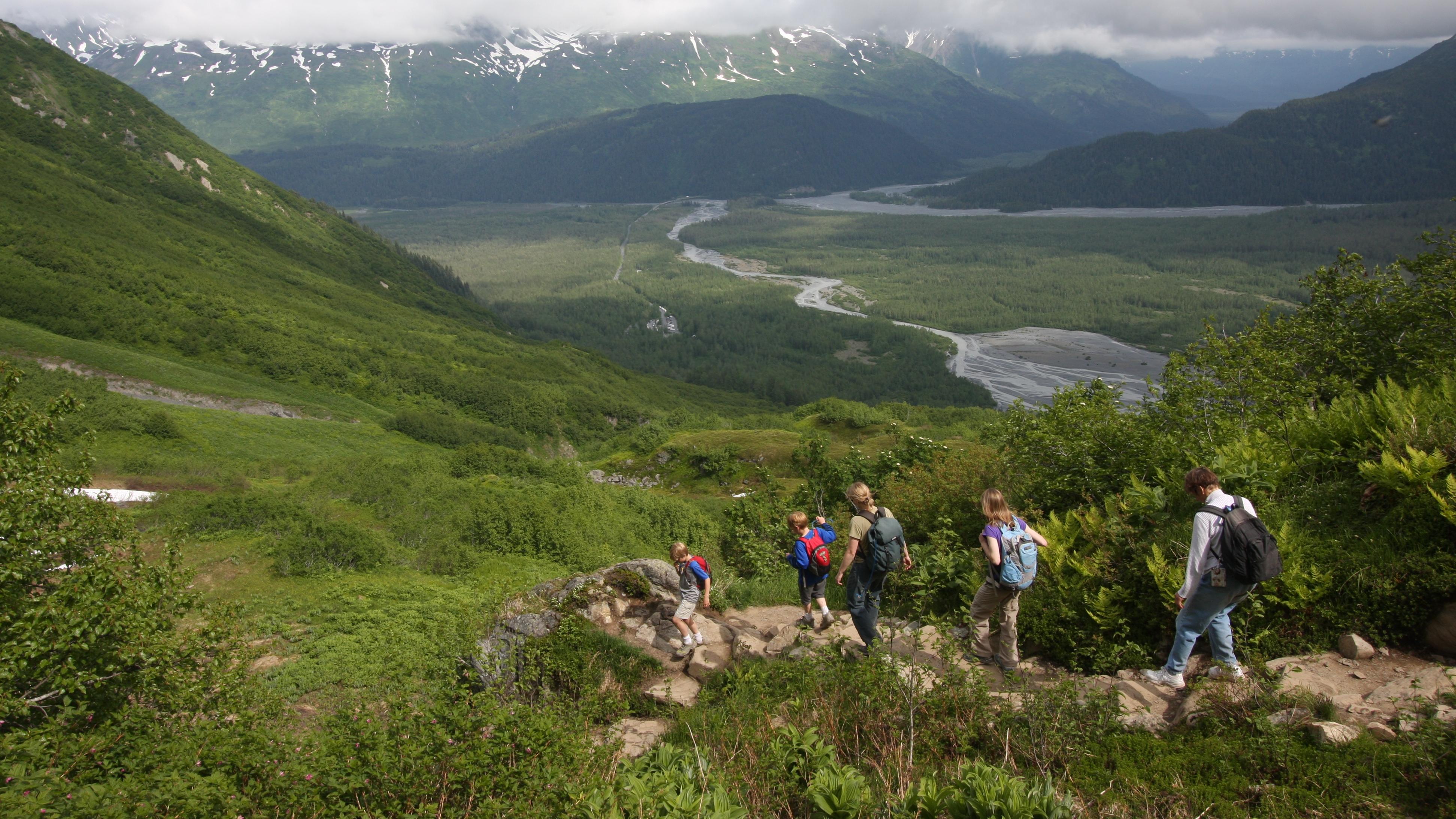 A group of people walking down a trail towards a valley