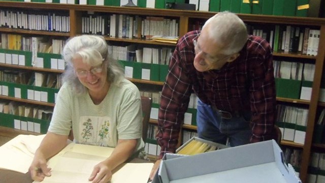 A man and a woman smiling as they review historical documents.
