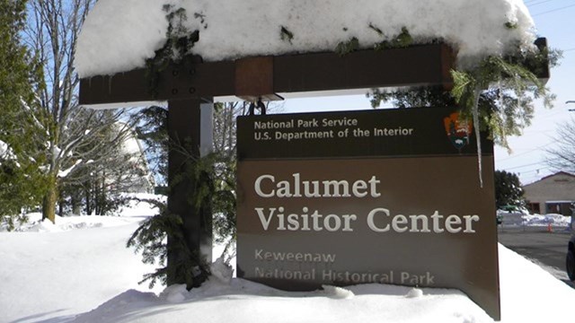 A visitor center sign is covered and almost buried in snow.