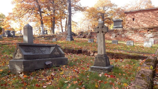 Grave markers are surrounded by a small masonry fence in a cemetery.