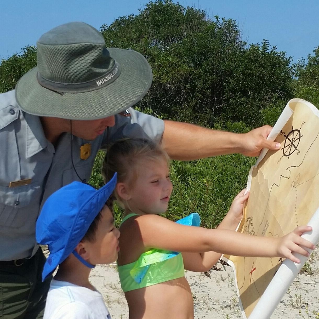 A male ranger points at a map while talking to a young boy and girl.