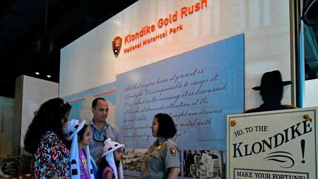 A ranger talks to a family in front of a museum welcome sign