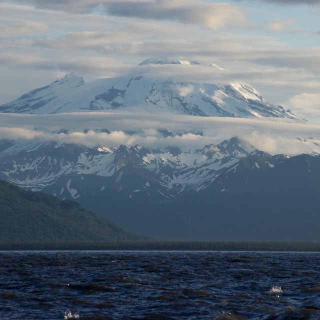 A ocean-side view of snowy Redoubt Volcano with clouds