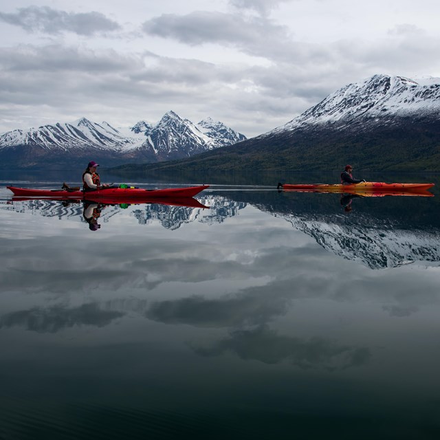 two kayaks on a still calm lake with snow covered mountains in background
