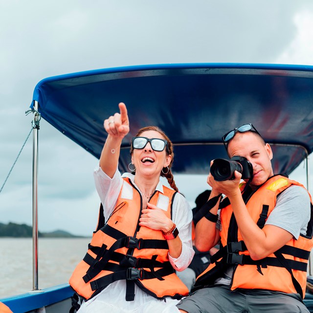 Two people enjoying a day on the lake, boating and taking pictures while wearing their PFDs.