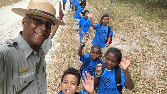 ranger takes selfie on trail with long line of kids wearing matching blue shirts and smiling