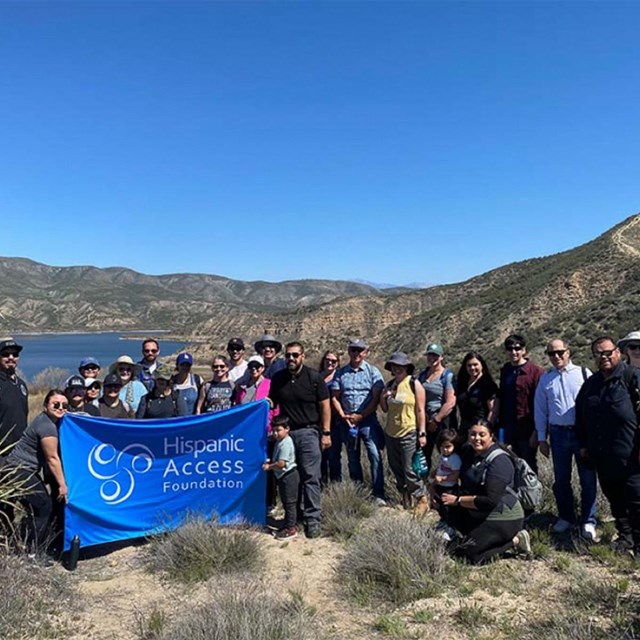 Group of people standing on a mountain top holding a blue Hispanic Access Foundation banner