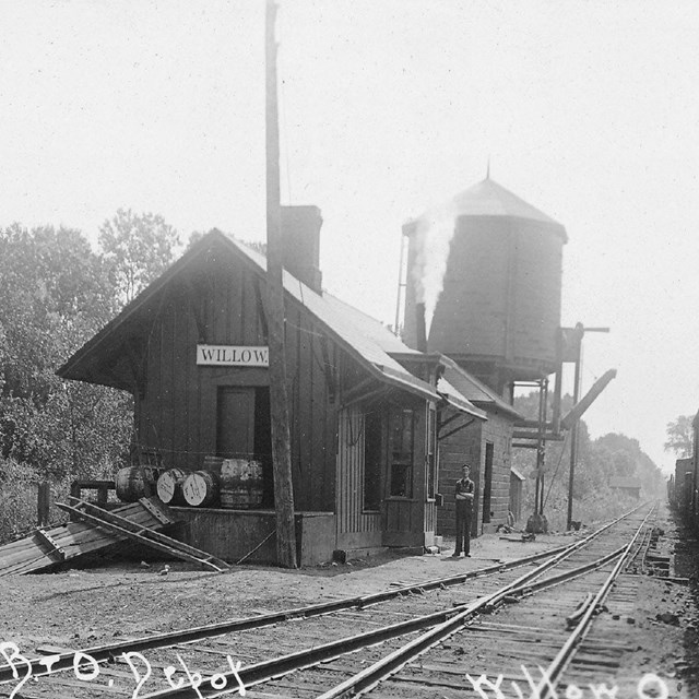 House next to railroad tracks with a food or water tank in the back