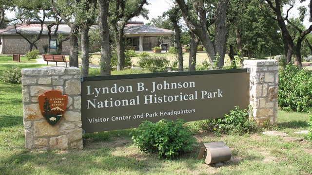 A large brown sign in front of a stone building reads "Lyndon B. Johnson National Historical Park."