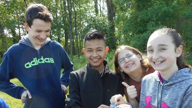 Four older children smiling for the camera while exploring outdoors 