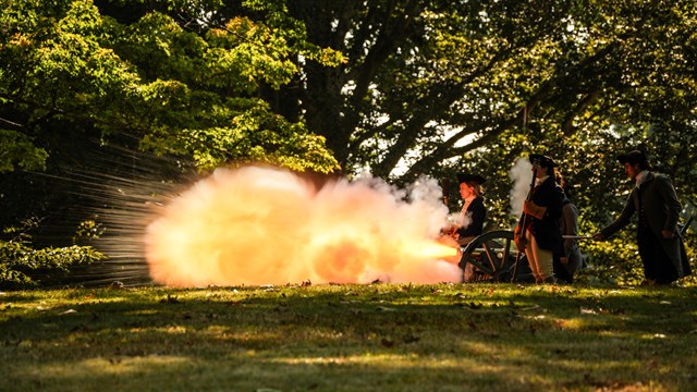 An 18th Century cannon fires and a flame shoots out of the gun.