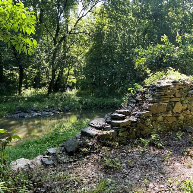 A ruined stone wall by a stream.