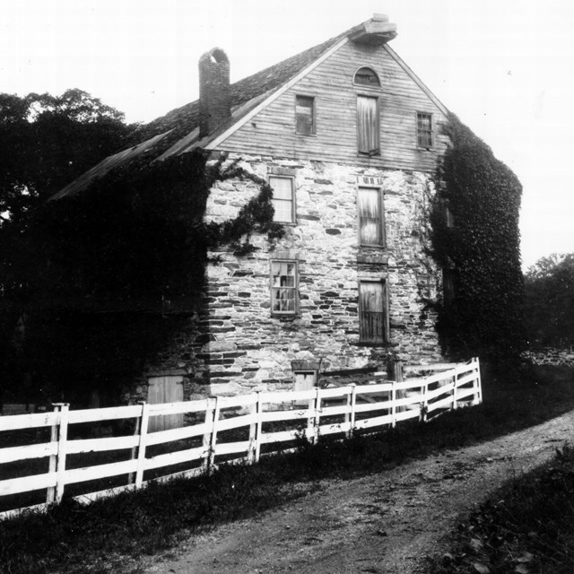 Black and white photo of a three-story stone mill with a road in front.