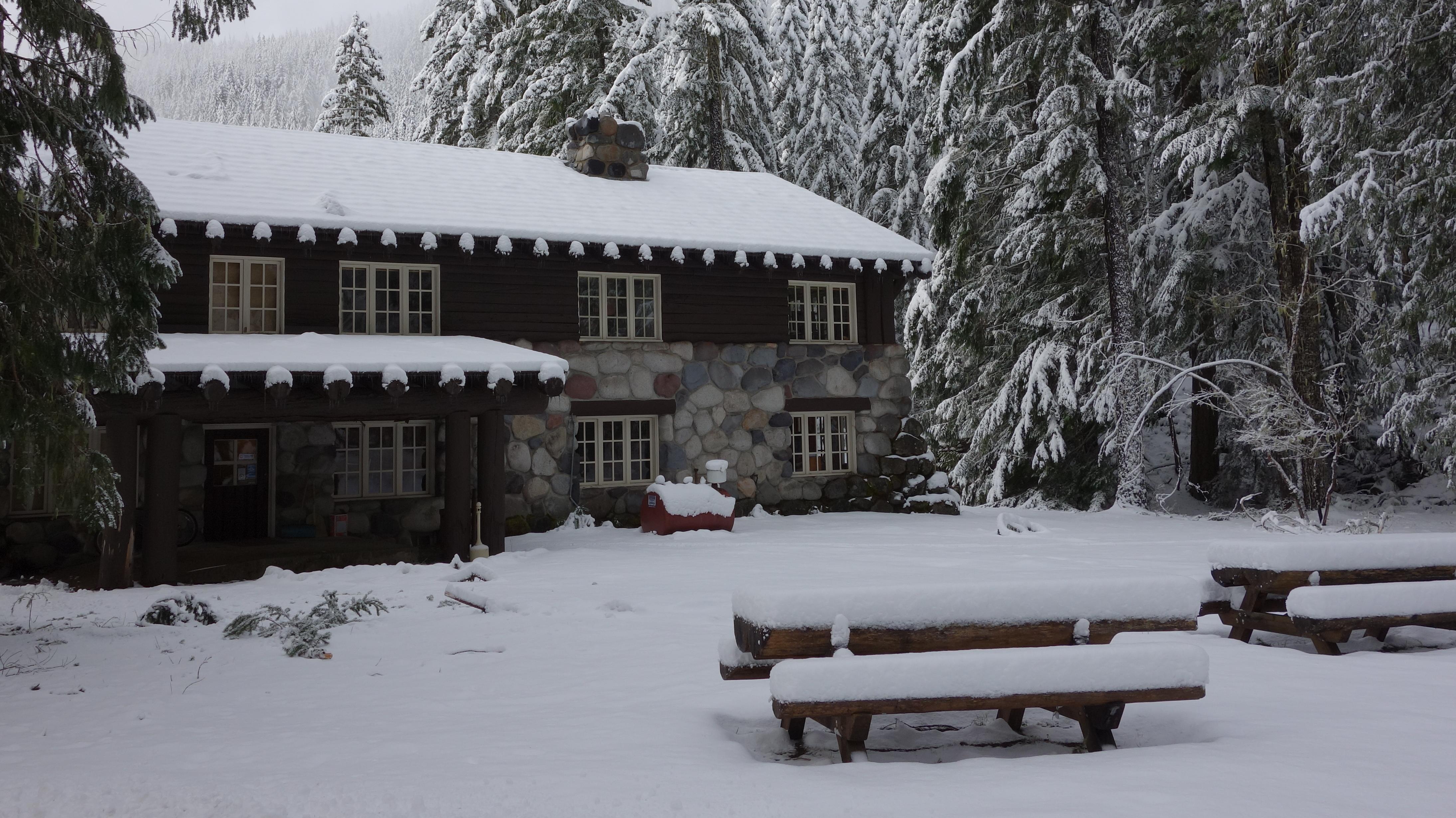 A wood and stone building tucked away in the forest and blanketed in snow. 