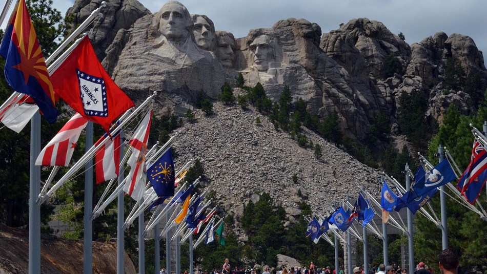 Visitors walk along the Avenue of Flags with Mount Rushmore in the background. 
