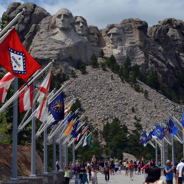 Photo of visitors walking through the Avenue of Flags with Mount Rushmore in the background.