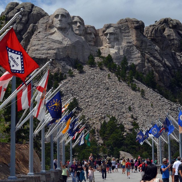 Visitors walking along the Avenue of Flags with Mount Rushmore in the background.