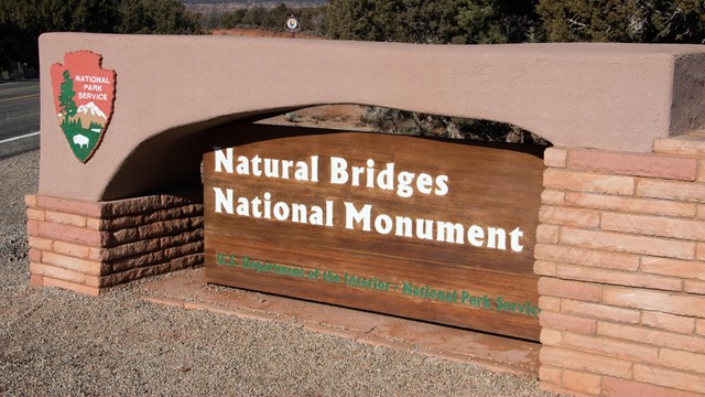 A sign with the NPS arrowhead reads Natural Bridges National Monument.