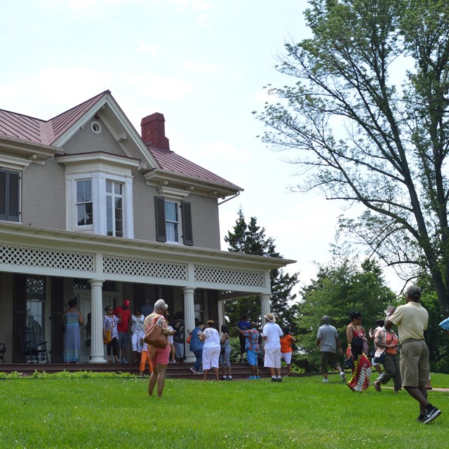 A historic house with a group of people standing on the front lawn